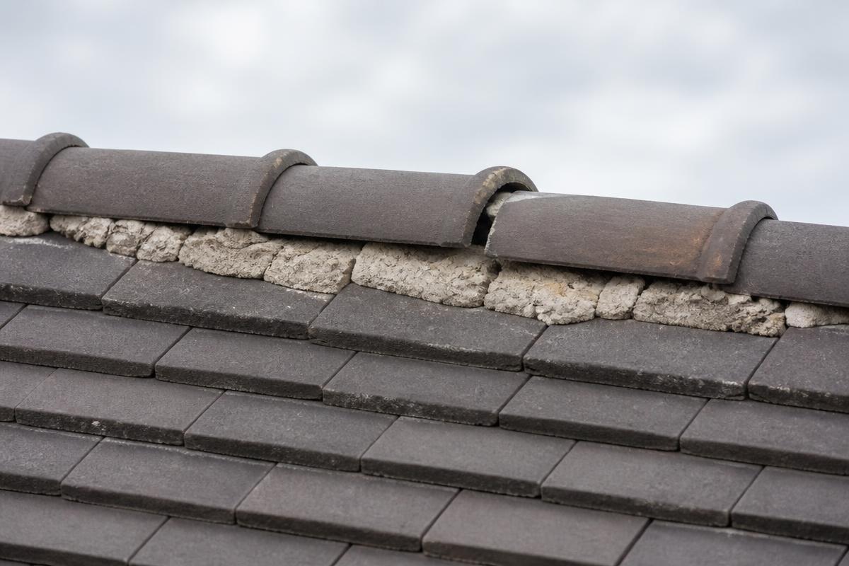 Ridge tiles along a roof apex with cracked mortar bedding and one tile out of line